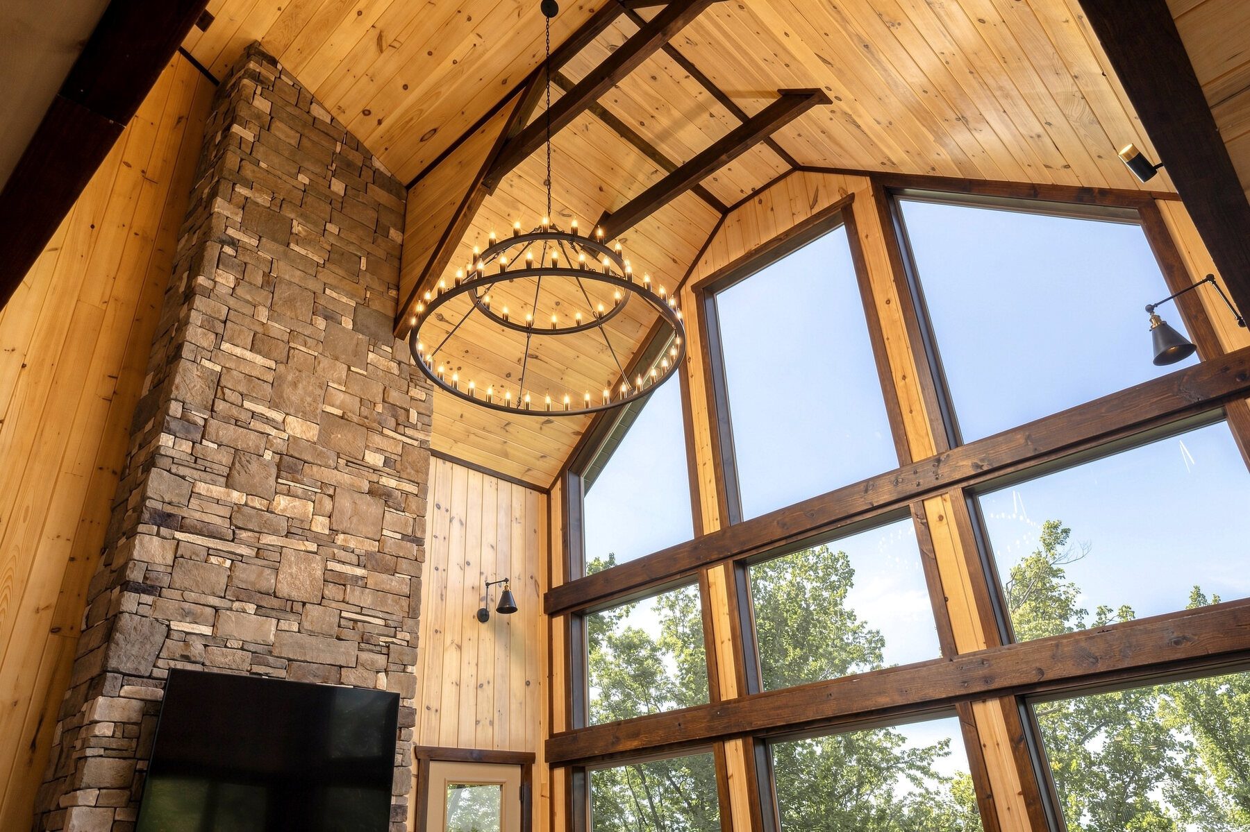 The stone fireplace and circular chandelier rising into the timber ceiling
